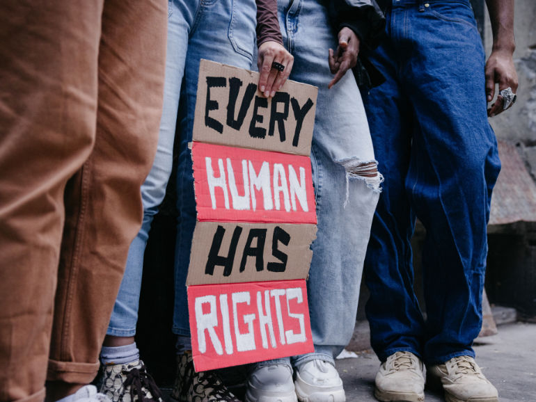 Four people standing, one holding a cardboard saying "Every human has rights"