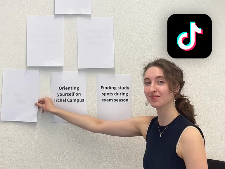 Eine Studentin steht vor einer Wand, an der sie verdeckte Papierbotschaften aufdeckt